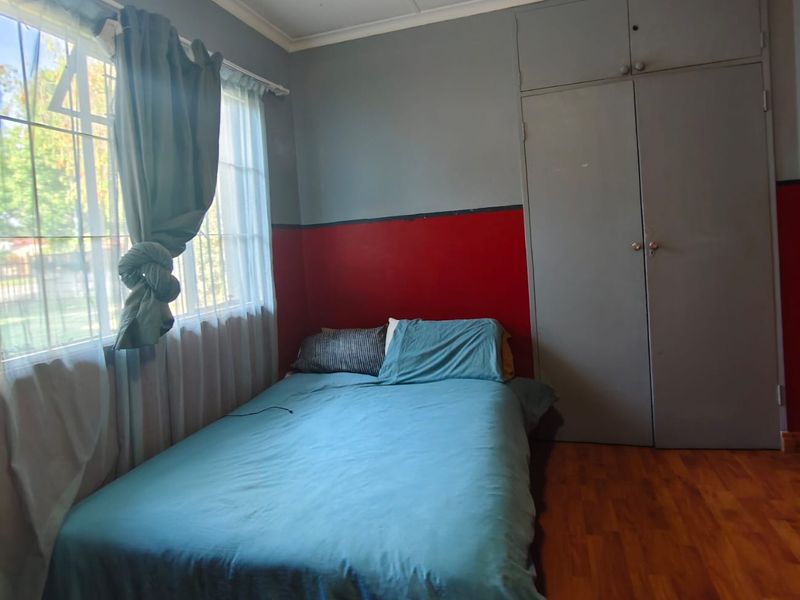 A bedroom featuring laminate flooring, built-in cupboards, and a ceiling fan, offering a functional space with potential for cosmetic updates.