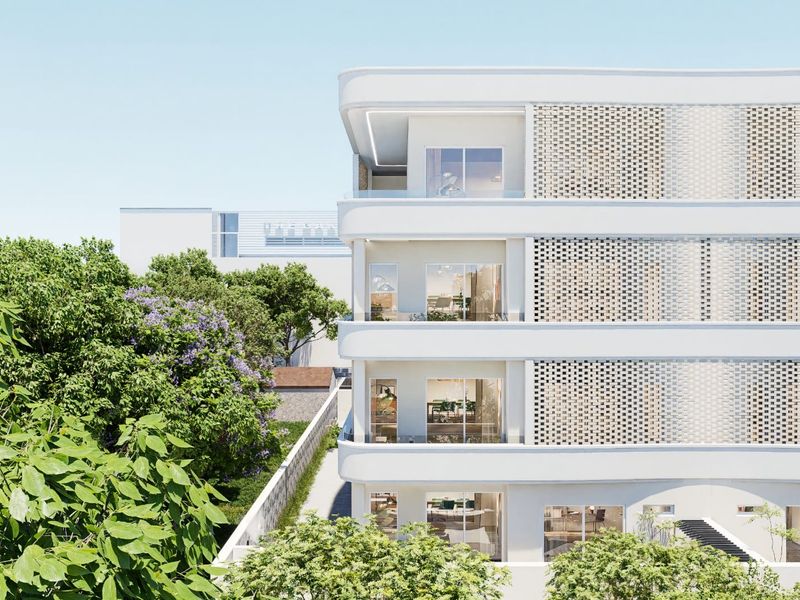 A modern apartment building facade featuring clean white lines, decorative brickwork screens, and private balconies with large sliding glass doors.
