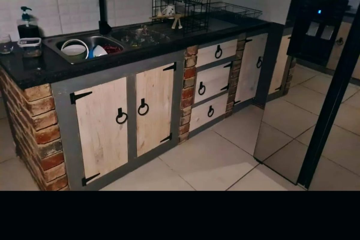 A rustic-style kitchen featuring exposed brick cabinetry bases, granite countertops, and a tiled backsplash with a functional sink area.