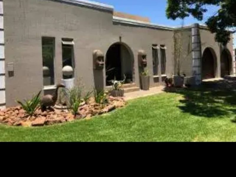 Front elevation of a single-story home featuring a plastered facade, arched entrance, and well-maintained garden area.