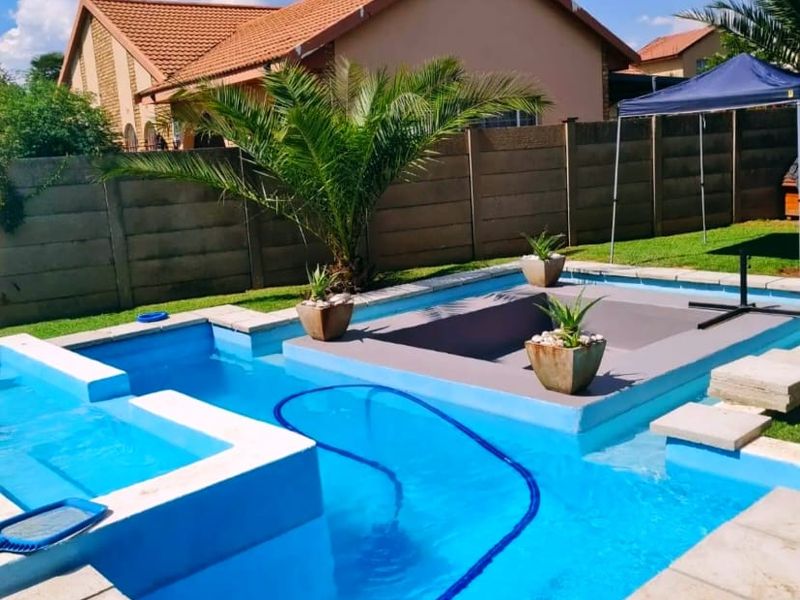 A well-maintained swimming pool area featuring a raised deck, tiled coping, and a secure precast concrete boundary wall in a private garden setting.