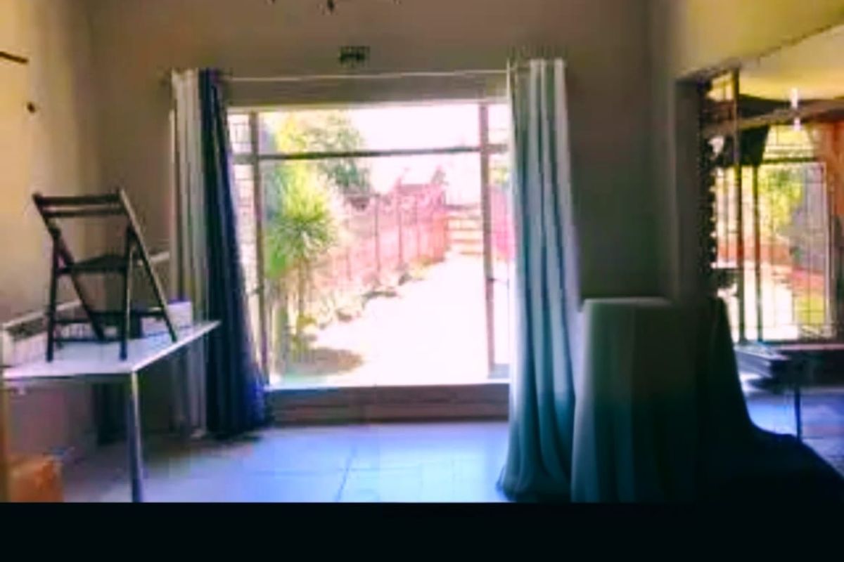 A living room area featuring tiled flooring and a large sliding glass door with security bars, providing access to the outdoor space.