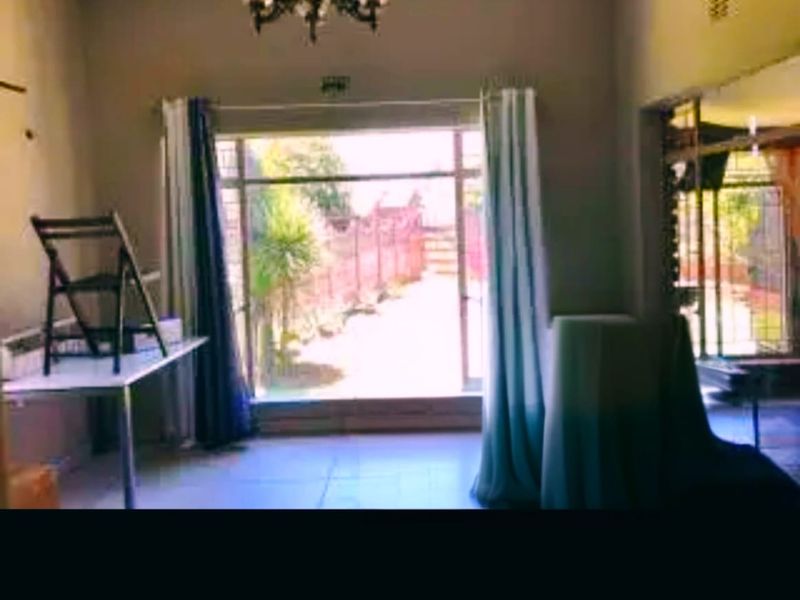 A living room area featuring tiled flooring and a large sliding glass door with security bars, providing access to the outdoor space.