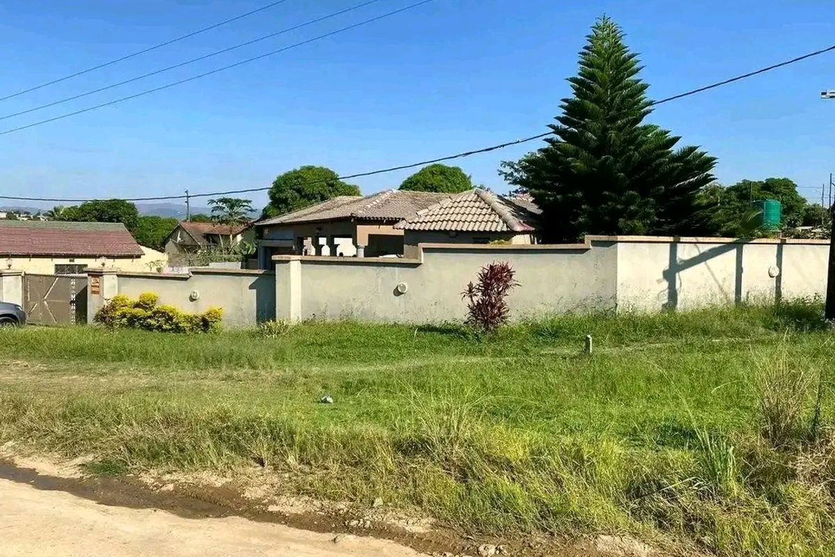 Front view of a residential property featuring a perimeter wall, tiled roof, and gated entrance, set on a grassed lot.