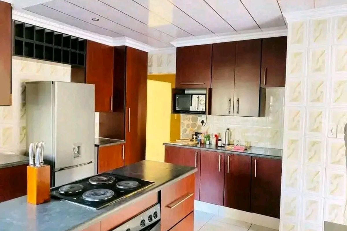 A functional kitchen featuring dark wood cabinetry, a central island with a built-in hob and oven, tiled flooring, and a tiled backsplash.
