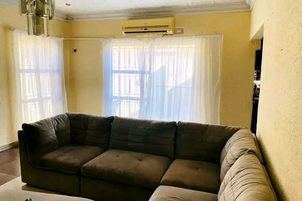A living room featuring tiled flooring, a wall-mounted air conditioning unit, and security bars on the windows.