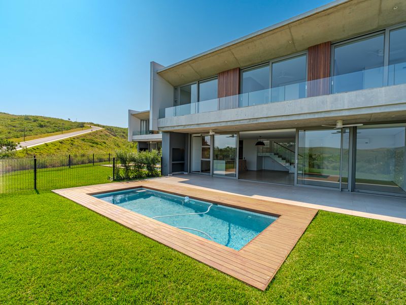 Modern architectural home featuring a swimming pool with timber decking, a spacious tiled patio, and large sliding glass doors opening to the interior.