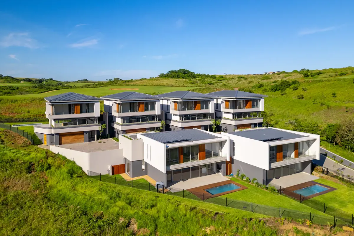 Aerial view of a modern residential complex featuring multiple units with private swimming pools, timber decks, and landscaped gardens set in a scenic landscape.