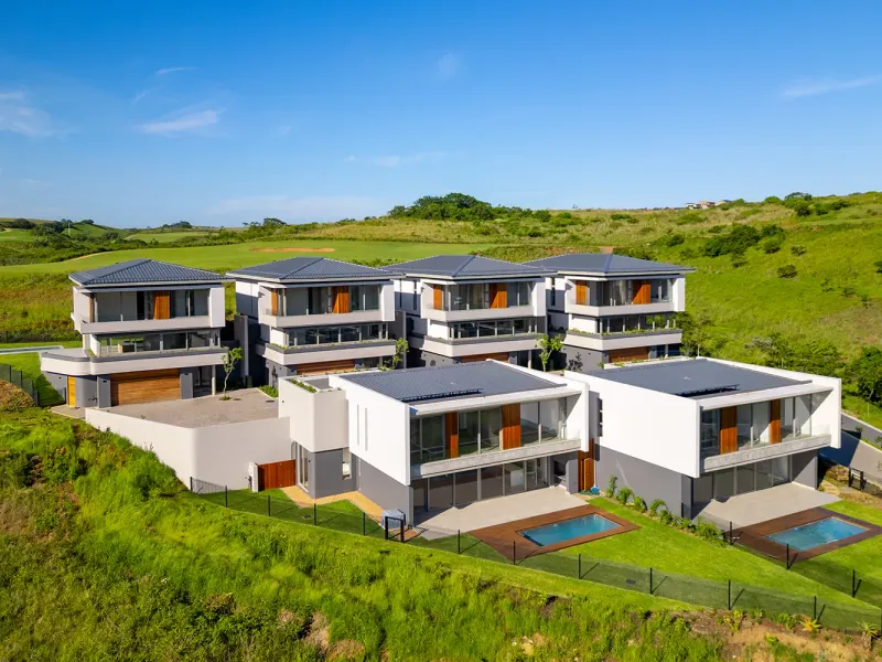 Aerial view of a modern residential complex featuring multiple units with private swimming pools, timber decks, and landscaped gardens set in a scenic landscape.