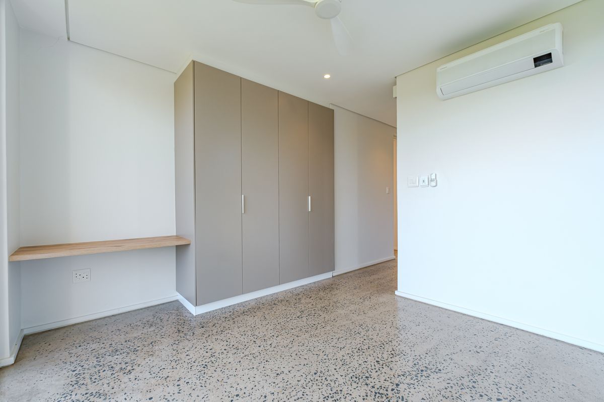 Modern bedroom featuring polished concrete floors, built-in cupboards, a floating desk, and a split-system air conditioner.