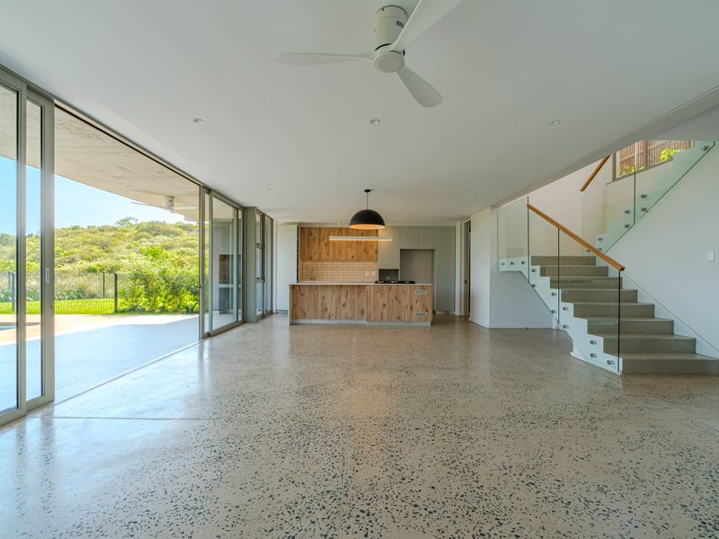 Spacious open-plan living area featuring polished concrete floors, a modern kitchen, and seamless indoor-outdoor flow through large sliding glass doors to the patio.