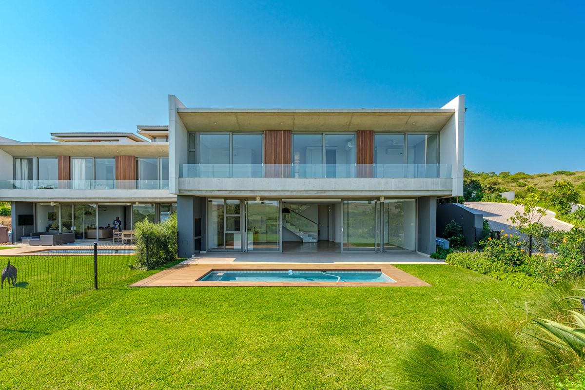 Modern double-story residence featuring a rear swimming pool, timber decking, expansive glass sliding doors, and a covered patio area overlooking the garden.