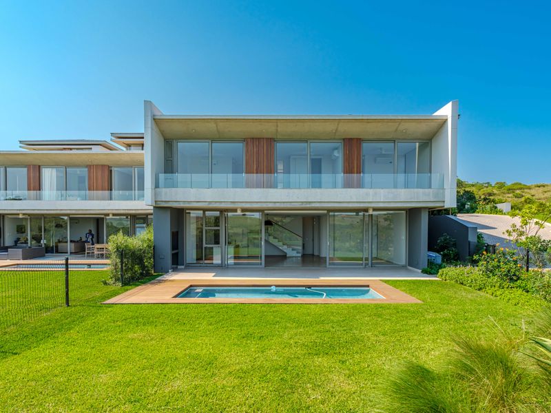 Modern double-story residence featuring a rear swimming pool, timber decking, expansive glass sliding doors, and a covered patio area overlooking the garden.