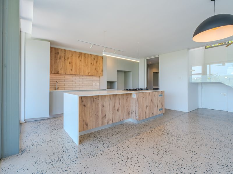 Modern open-plan kitchen featuring a central island with wood-grain cabinetry, stone countertops, gas hob, and polished concrete flooring, seamlessly integrated into the living space.