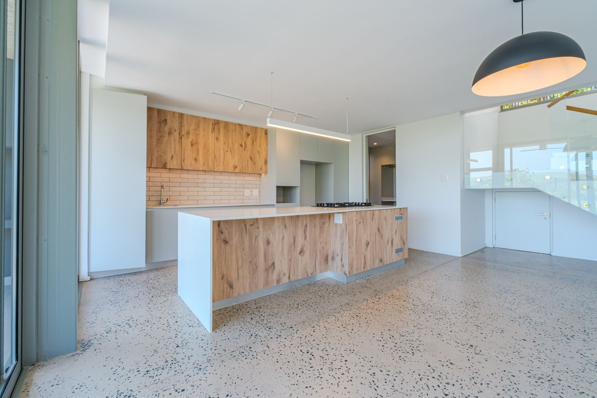 Modern open-plan kitchen featuring a central island with wood-grain cabinetry, stone countertops, gas hob, and polished concrete flooring, seamlessly integrated into the living space.