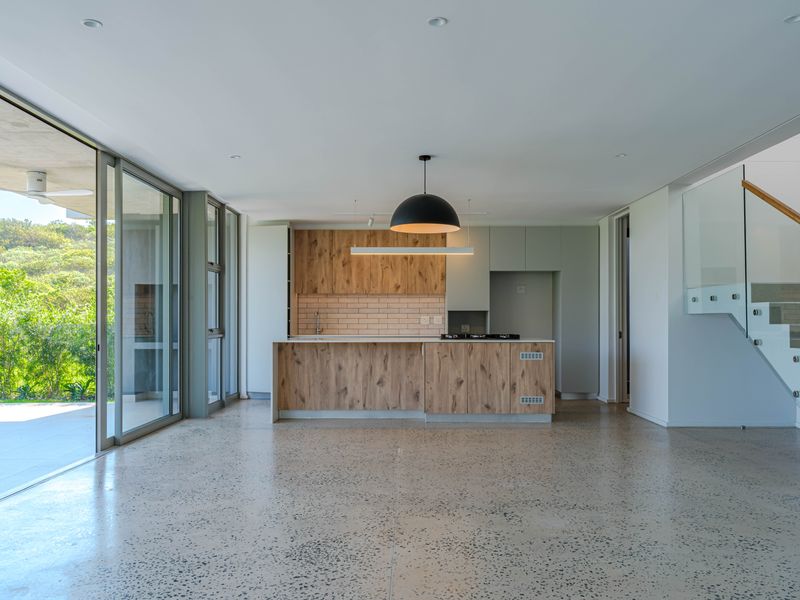 Modern open-plan kitchen and living area featuring polished concrete floors, wood-finish cabinetry, and large sliding doors opening to a garden view.