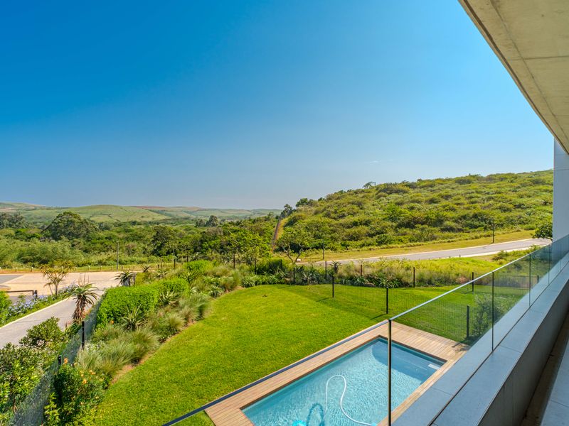 Elevated view from a balcony overlooking a private swimming pool, landscaped garden, and scenic rolling hills.
