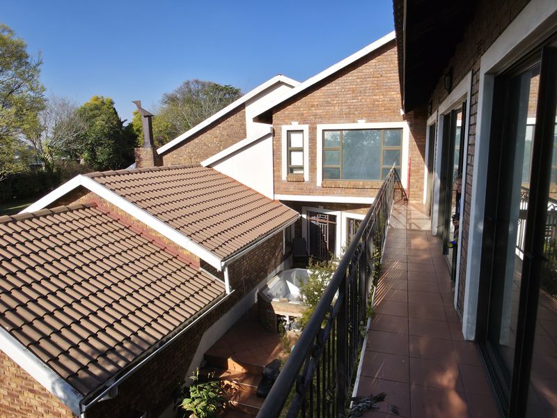 An elevated tiled balcony with wrought iron railings, offering views over the property's brick-clad exterior and tiled roof sections.