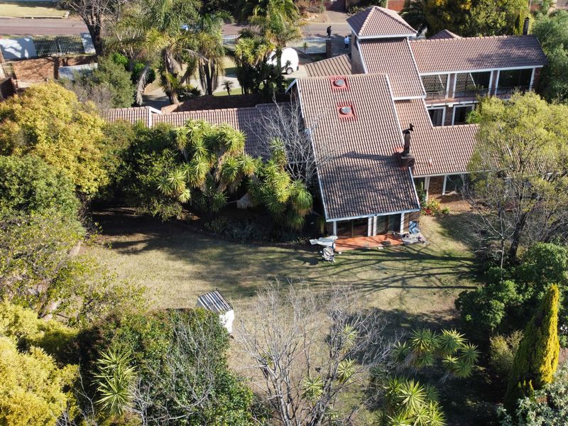 Aerial view of a residential property featuring a tiled roof, chimney, and a spacious garden with mature trees and a patio area.