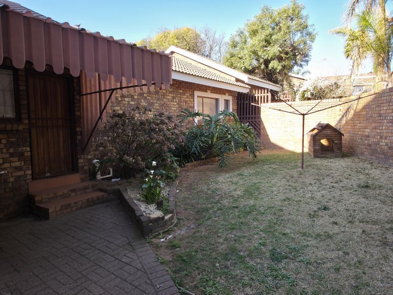 A private rear garden featuring a paved patio area, brick boundary walls, and a metal awning over the entrance.