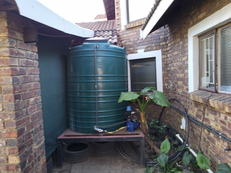Rear exterior area featuring a green water storage tank with an integrated pump system, set against a brick building facade.