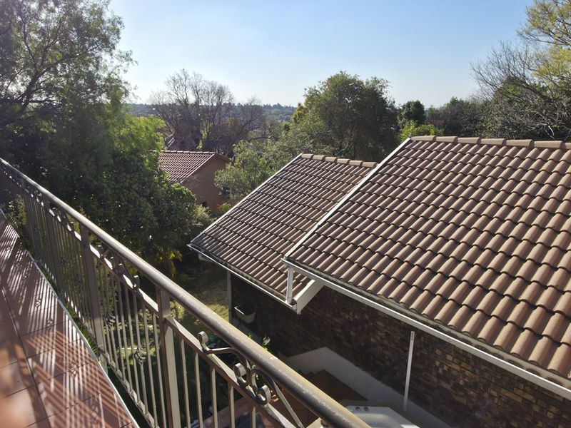 An elevated balcony featuring tiled flooring and a metal balustrade, overlooking the property's tiled roof and surrounding garden area.