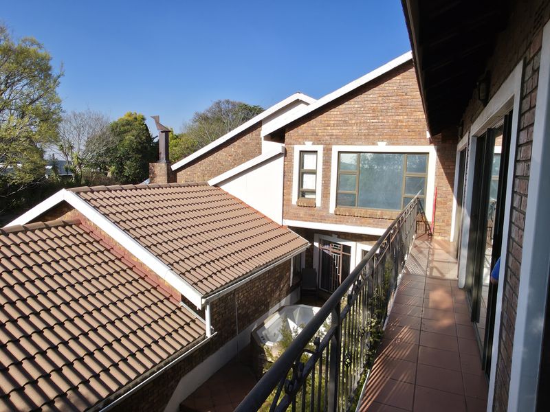An elevated balcony with wrought iron railings and tiled flooring, overlooking the rear garden and adjacent roof structures.