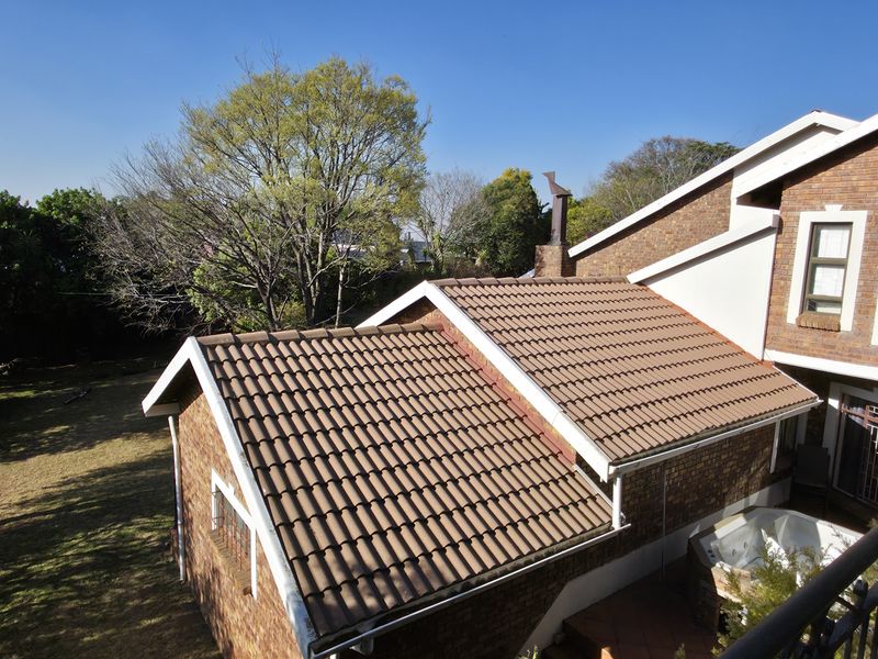 An elevated view of the rear exterior featuring a brick facade, tiled roof sections, and a balcony with wrought iron railings overlooking the garden.