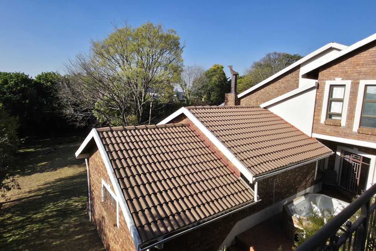 An elevated view of the rear exterior featuring a brick facade, tiled roof sections, and a balcony with wrought iron railings overlooking the garden.