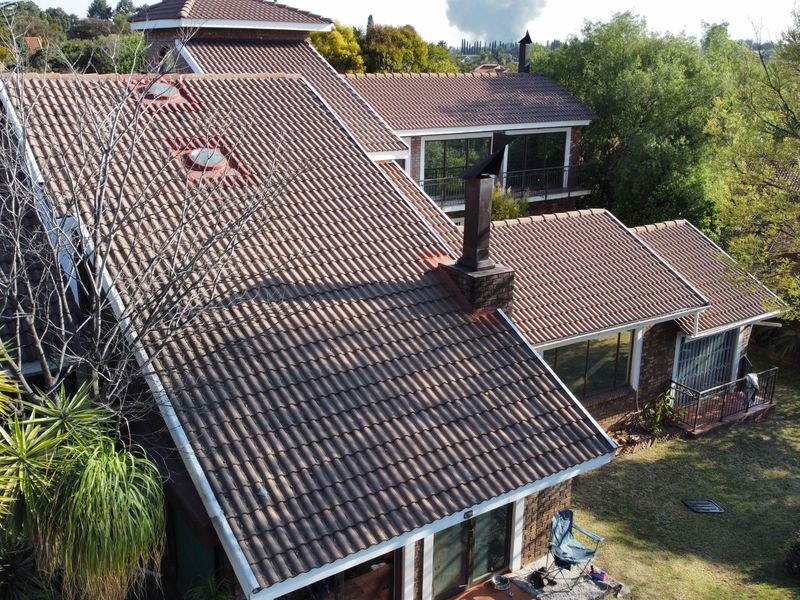 Aerial view of a multi-level residential property featuring a tiled roof, brick chimney, skylights, and an upper-level balcony overlooking the garden.