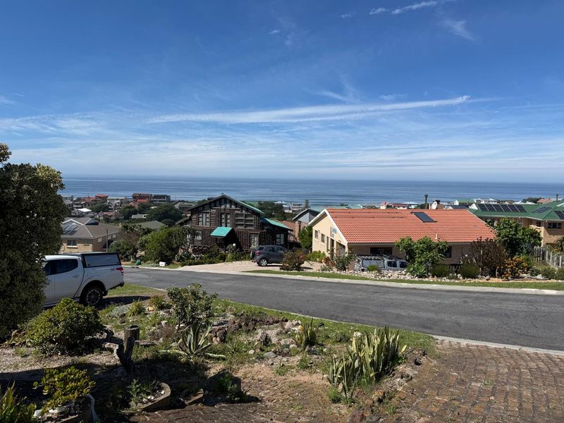 A scenic elevated view overlooking a coastal residential neighbourhood with the ocean visible in the distance under a clear blue sky.