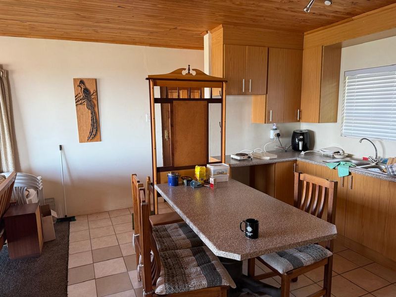 Open-plan kitchen and dining area featuring timber ceiling, laminate cabinetry, stone-look countertops, and tiled flooring.