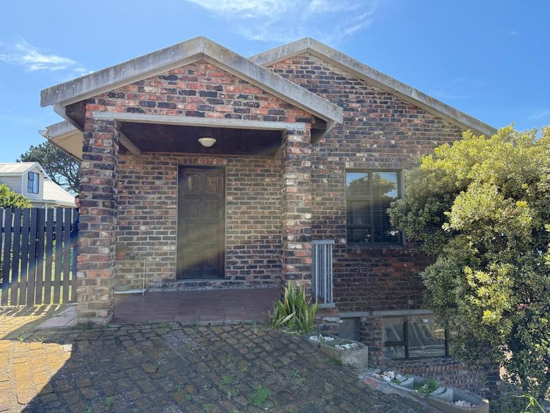 Front elevation of a face-brick flat featuring a covered entrance porch, paved driveway, and established garden elements.