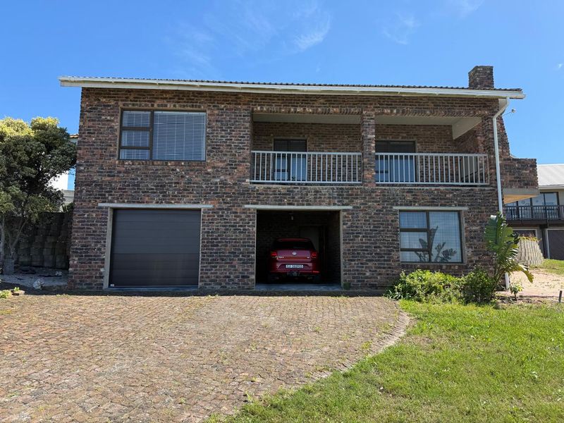A double-story face brick residential property featuring a garage, a covered carport, and an upper-level balcony with a paved driveway approach.