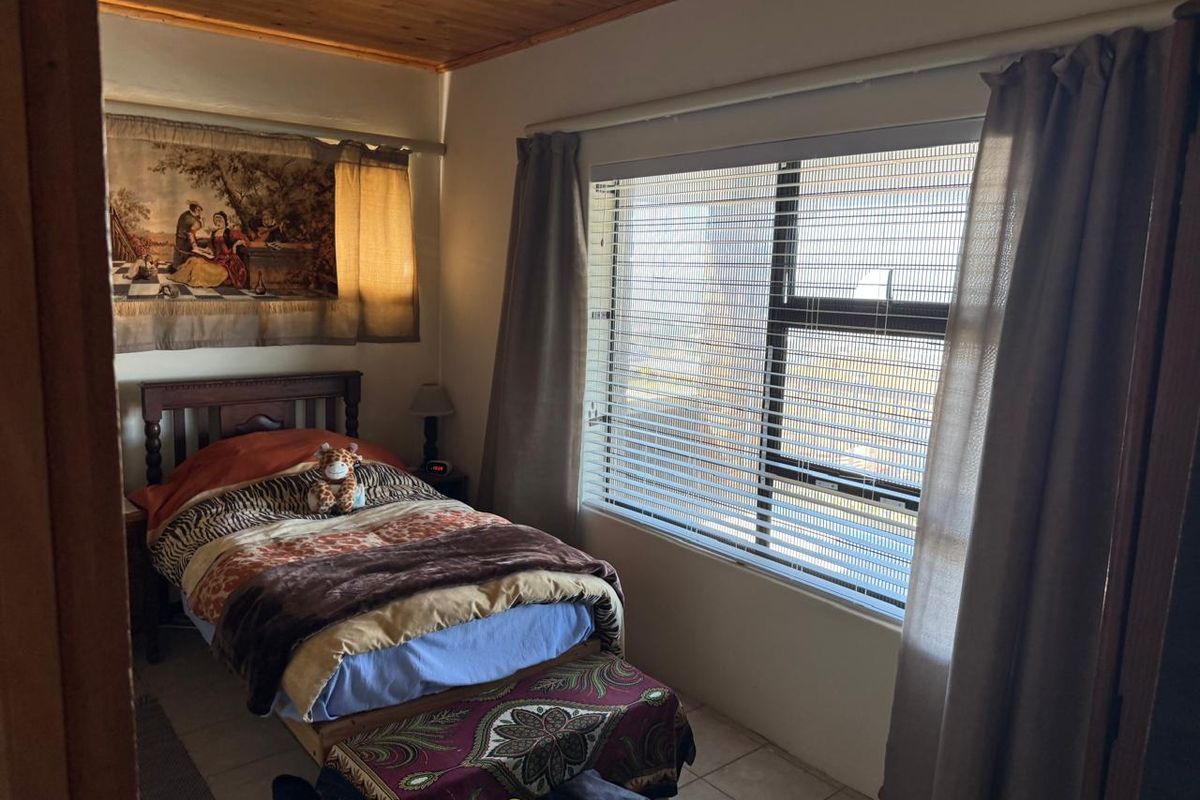 A bedroom featuring tiled flooring, a timber-clad ceiling, and an aluminium-framed window with fitted venetian blinds.