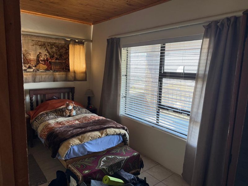 A bedroom featuring tiled flooring, a timber-clad ceiling, and an aluminium-framed window with fitted venetian blinds.