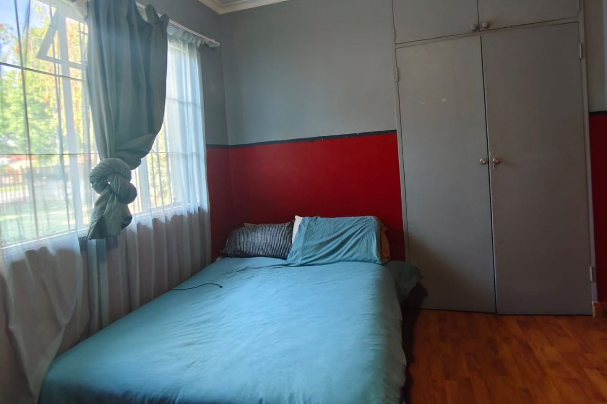 A bedroom featuring laminate flooring, built-in cupboards, and a ceiling fan, offering a functional space with potential for cosmetic updates.