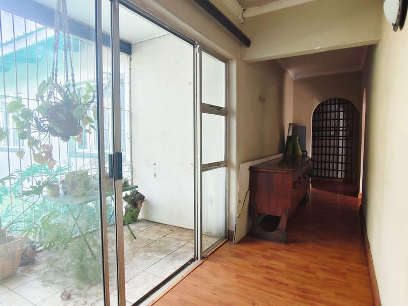 A hallway featuring laminate flooring and a large sliding glass door leading to an outdoor patio area, with visible ceiling maintenance required.
