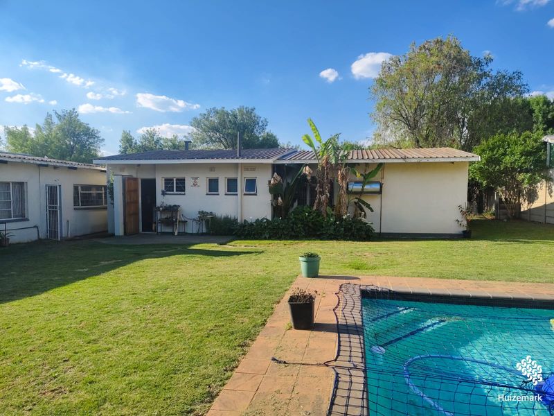Rear view of the property featuring a swimming pool with a paved surround, a well-maintained lawn, and a solar geyser installed on the roof.