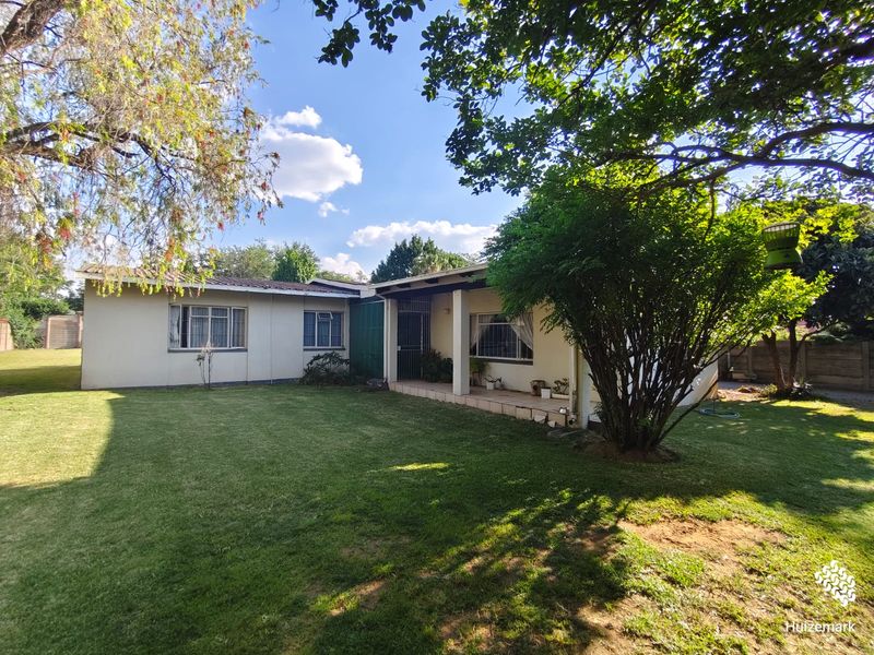 Rear view of the house featuring a covered patio area, established garden, and well-maintained exterior walls with metal-framed windows.
