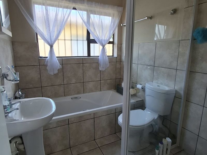 A functional bathroom featuring a pedestal basin, bathtub, and a separate glass-enclosed shower with neutral wall and floor tiling.