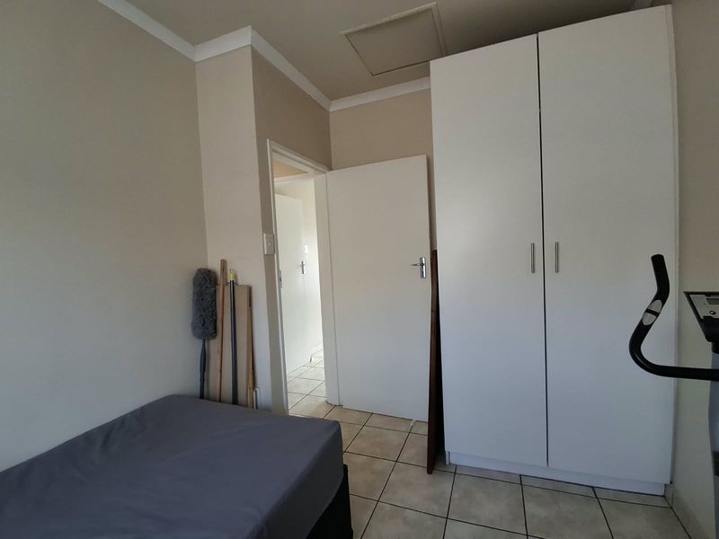A functional bedroom featuring tiled flooring, a built-in wardrobe, and a ceiling access hatch, providing a clean and practical living space.