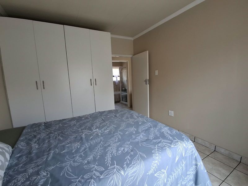 A bedroom featuring built-in cupboards, tiled flooring, and an adjoining bathroom entrance.