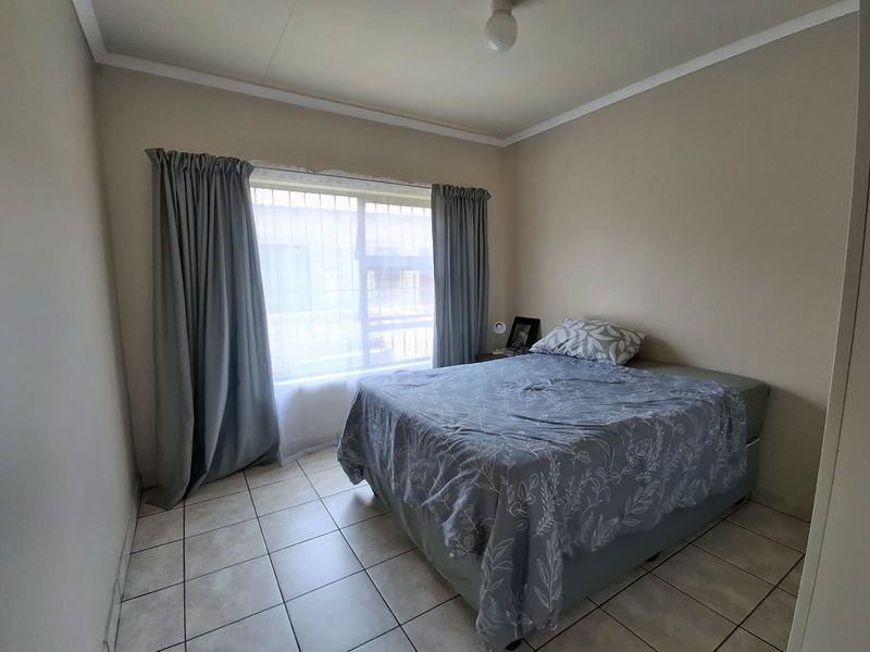 A functional bedroom featuring tiled flooring and a window fitted with security bars, providing a neutral space ready for personalization.