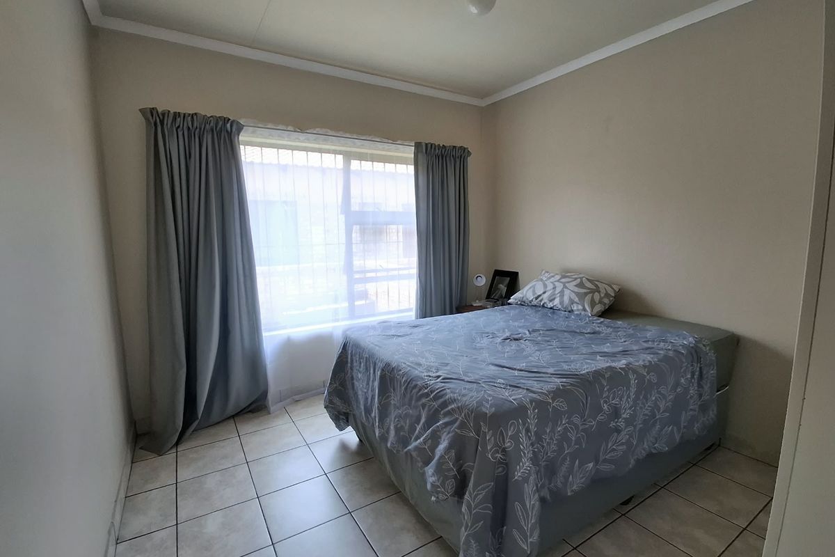 A functional bedroom featuring tiled flooring and a window fitted with security bars, providing a neutral space ready for personalization.