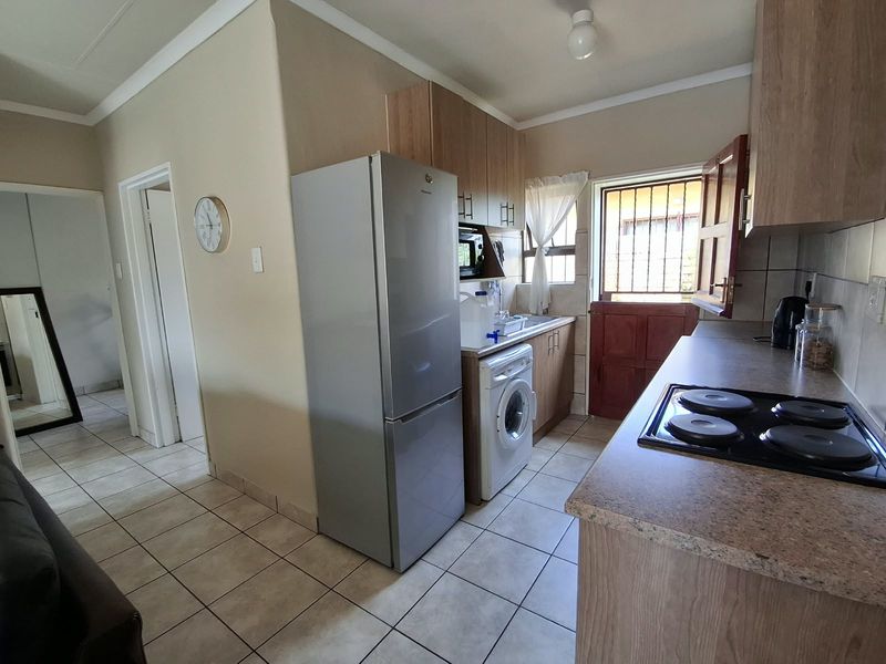Functional kitchen featuring wood-look cabinetry, laminate countertops, an electric hob, and tiled flooring with direct access to the exterior via a stable door.