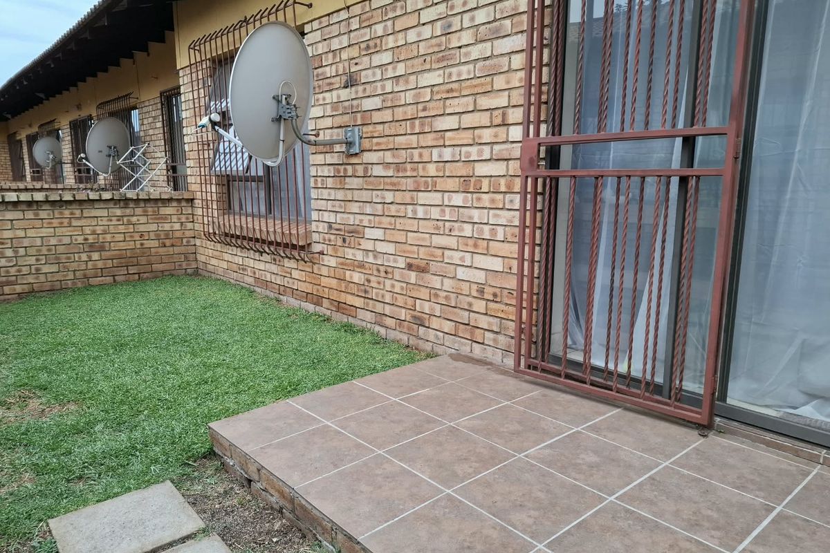 Rear exterior view of the townhouse featuring a tiled patio, brick facade, and security-fitted sliding doors leading to a small garden area.
