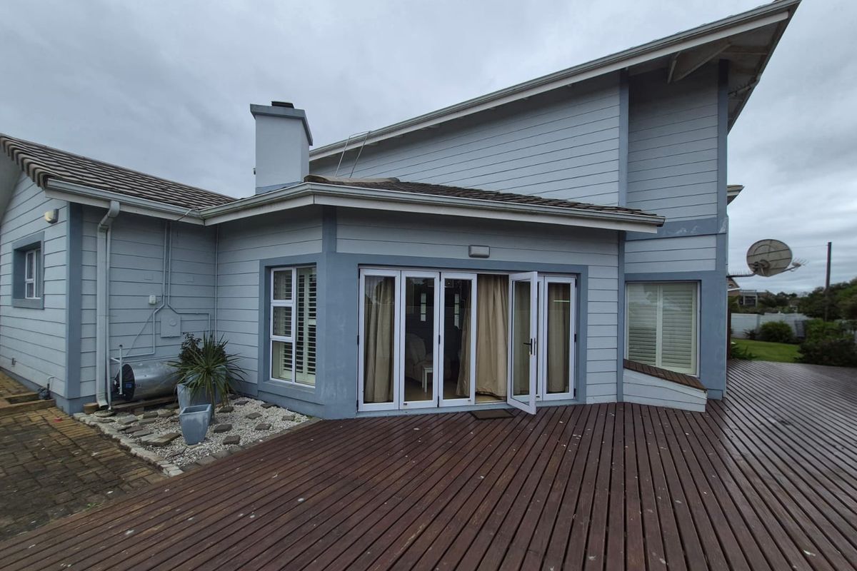 Rear exterior view featuring a spacious timber deck, bi-fold doors providing indoor-outdoor flow, and weatherboard cladding.
