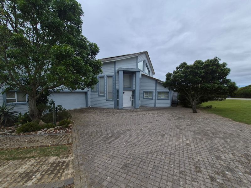 Front elevation of a multi-level house featuring timber cladding, a pitched roof, and a paved driveway leading to a double garage.
