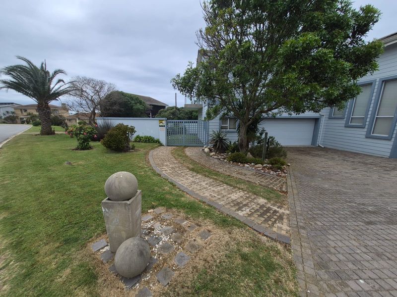 Front exterior view featuring a paved driveway, brick pathway, landscaped garden, and secure gated entrance to the property.